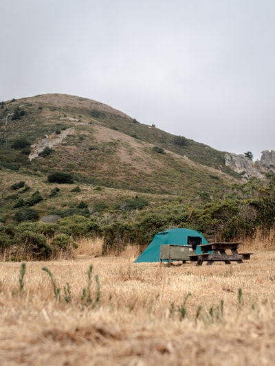 白天在山附近的绿草地上搭建蓝绿色帐篷